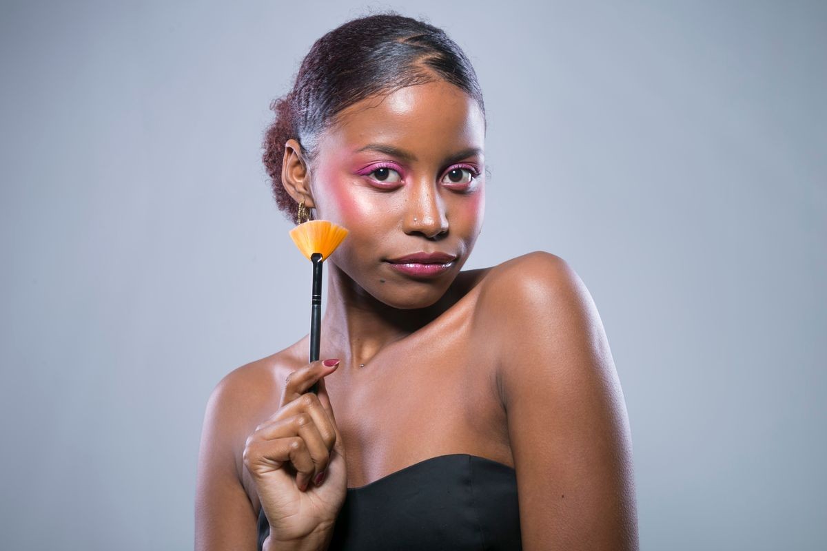 Young African woman in Studio doing body care and applying makeup, powder and rouge with a brush for young and beautiful skin